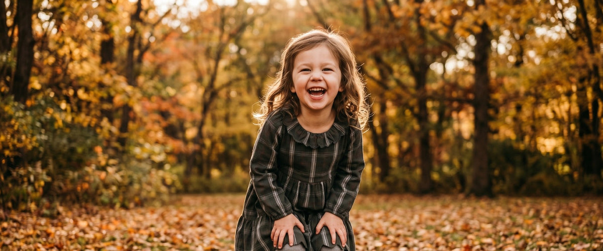 Smiling girl in a plaid dress standing in fall leaves